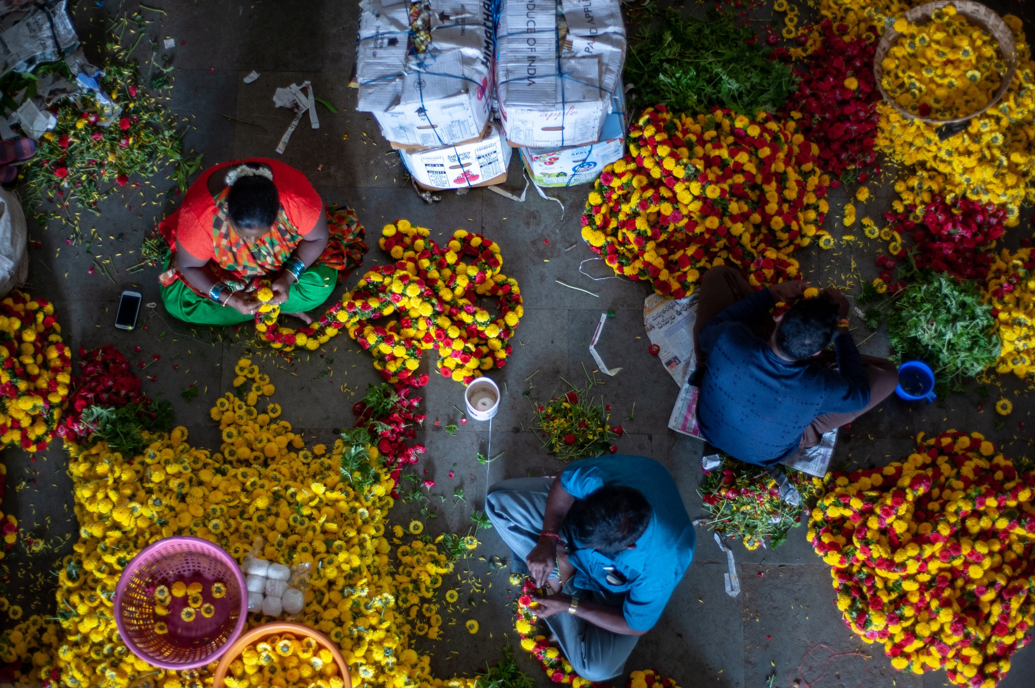 A top shot of three people who are working with individual marigold flowers to create garlands at Bangalore's KR Market. 