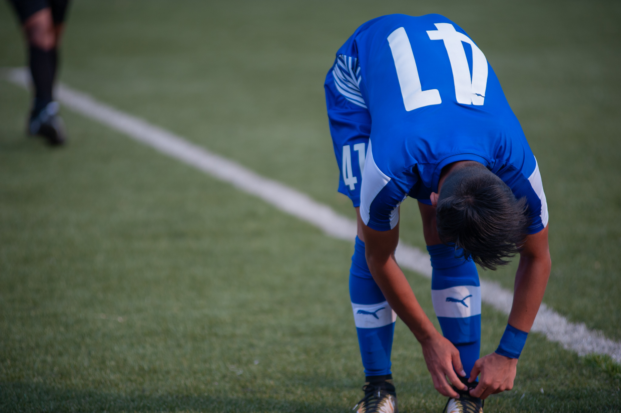 Naorem Roshan, the number 47 of Bengaluru FC, catches his breath and ties his shoelaces after the ball goes out for a goal kick.
