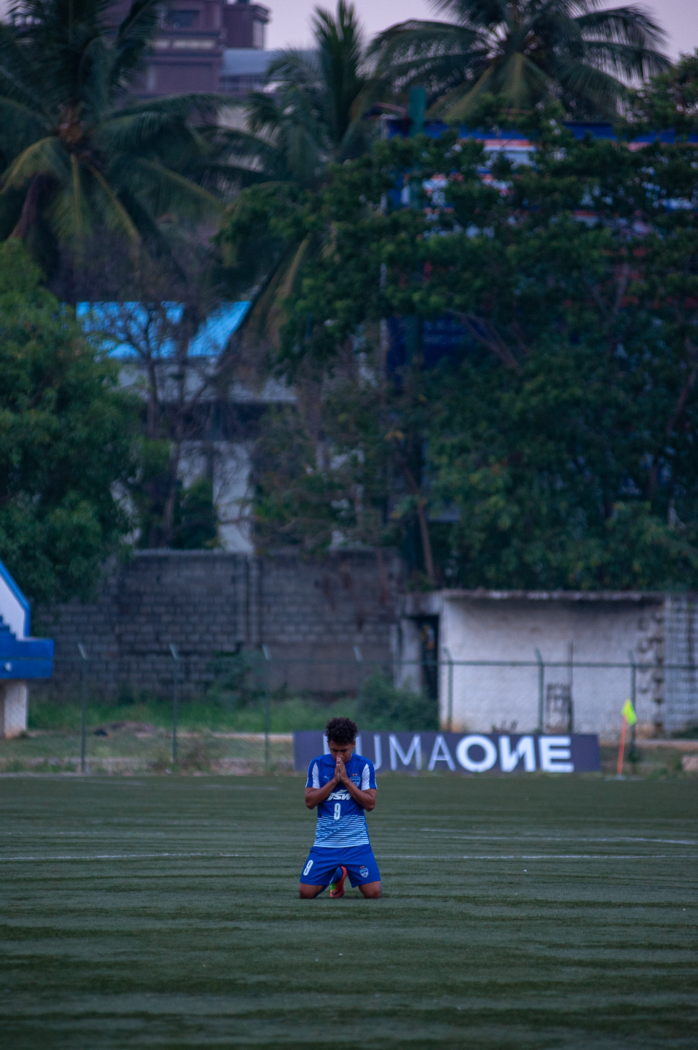 A Bengaluru FC B player is on his knees, hands folded in prayer, after the referee blows the final whistle. The Blues won the game 2 goals to one.