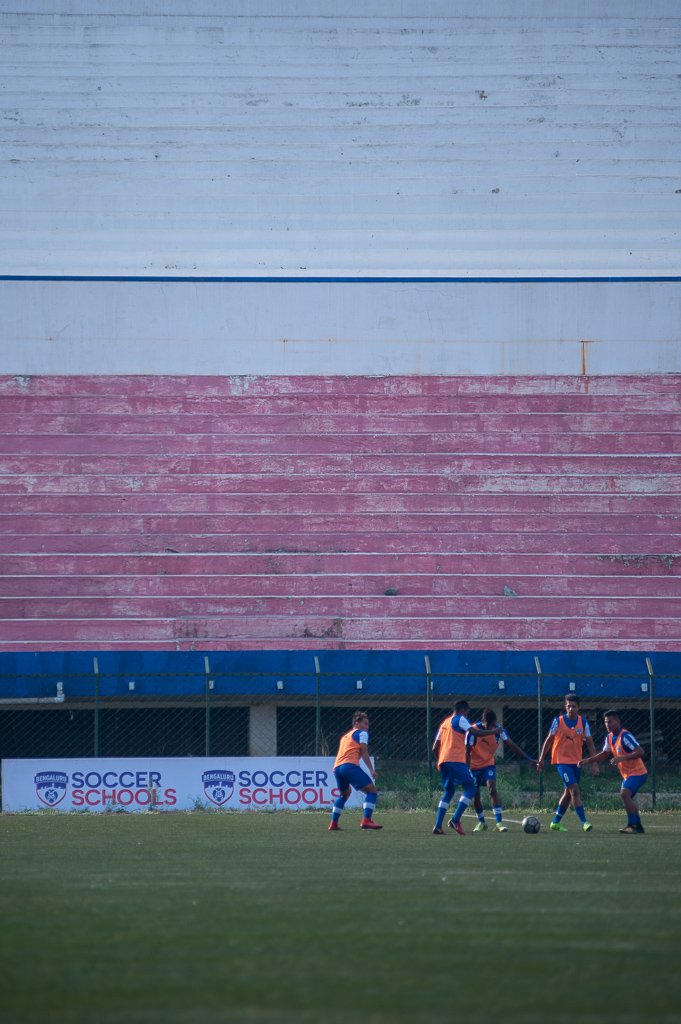 BFC B's substitutes warm up before an advertising board for Bengaluru FC's Soccer Schools.