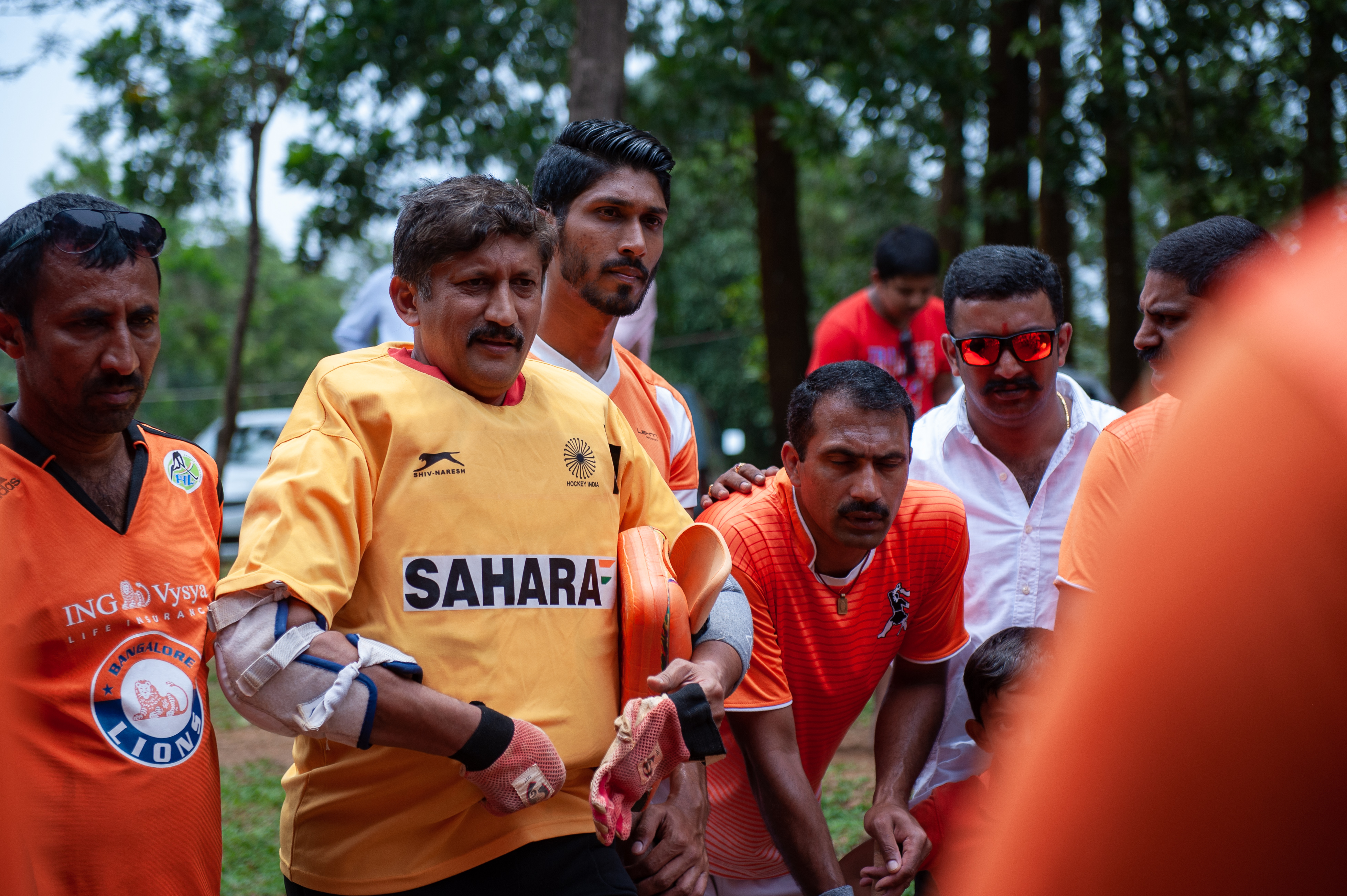 Dr. A B Subbaiah, goalkeeper of the Anjaparvanda, dressed in an India jersey, is seen giving a pep talk to his teammates before the start of the game. 