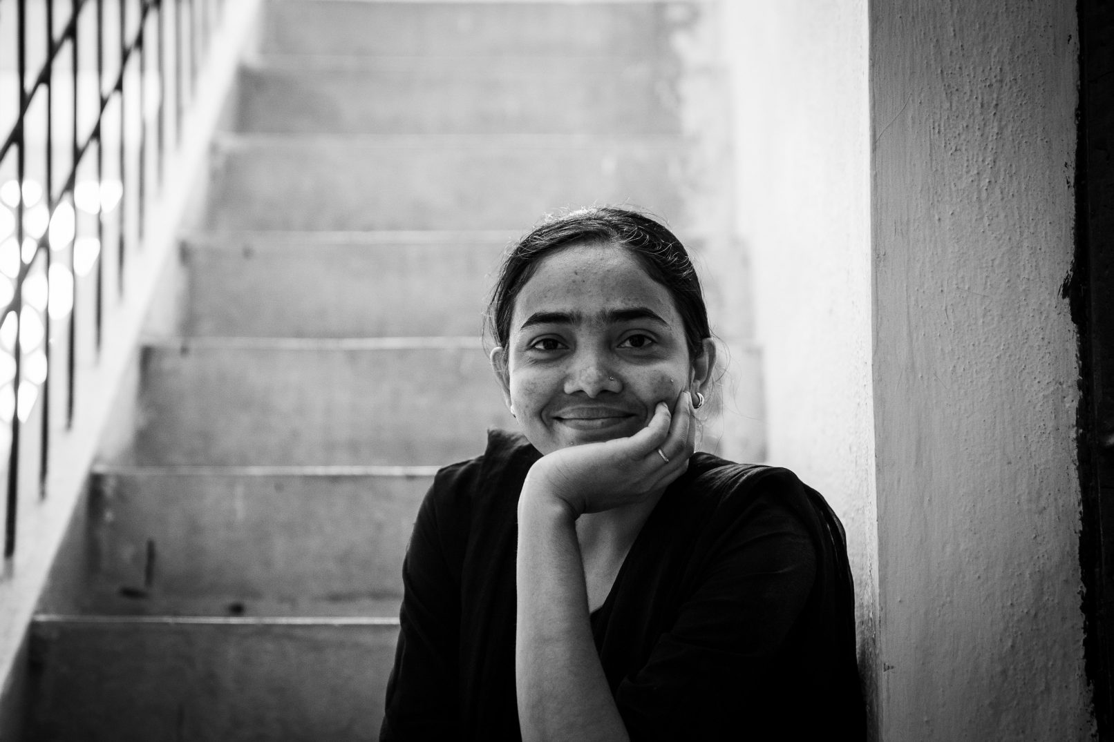 Tejusing Seema Pawar, hearing impaired since birth, who works at the Amazon FC in Bangalore, is seen looking at the camera, shot in a candid mood. The black and white image has her looking at the camera with her hand supporting her chin. She is seated on the stairs that lead up to her home. Shot for the company's #SheIsAmazon campaign.